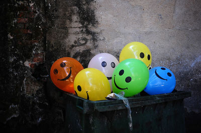 Anthropomorphic smiley face balloons in box against wall