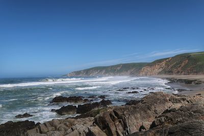 Landscape of rocks, sand, waves, water and green hills