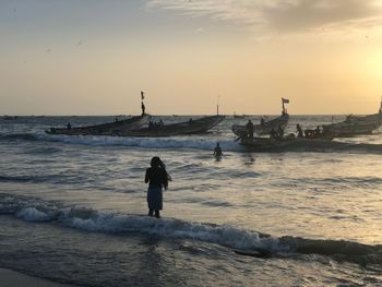 Rear view of woman standing in sea against sky during sunset