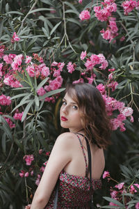 Portrait of young woman standing near oleander flower