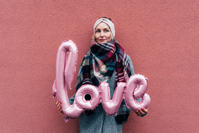 Woman holding love text balloon against wall