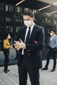 Businessman with face mask washing hands with hand sanitiser