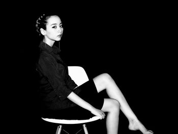 Woman sitting on chair against black background