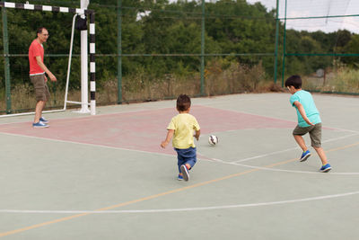 Sons playing soccer with father on court