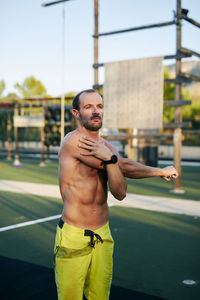 Shirtless fit young man stretching at outdoors gym military camp