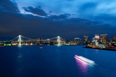 Illuminated bridge over river in city against sky at night