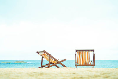 Deck chairs at beach against sky