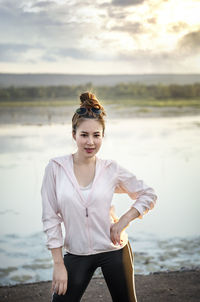 Young woman standing at beach against sky during sunset