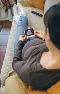 High angle view of woman holding ultrasound while sitting on sofa at home