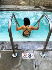 Rear view of woman sitting in swimming pool