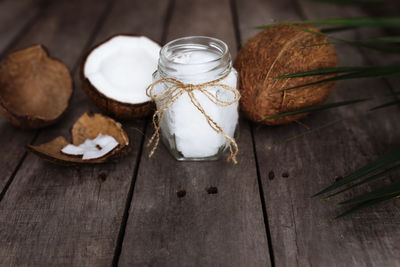 Broken coconuts on gray wooden background with jar of raw organic extra virgin oil, palm leaf