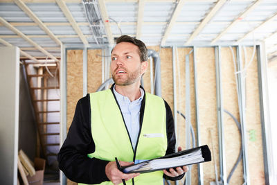 Thoughtful architect with file standing at construction site