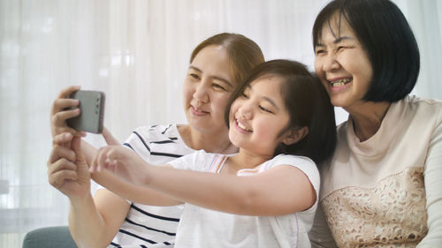 Smiling girl taking selfie with mother and grandmother at home