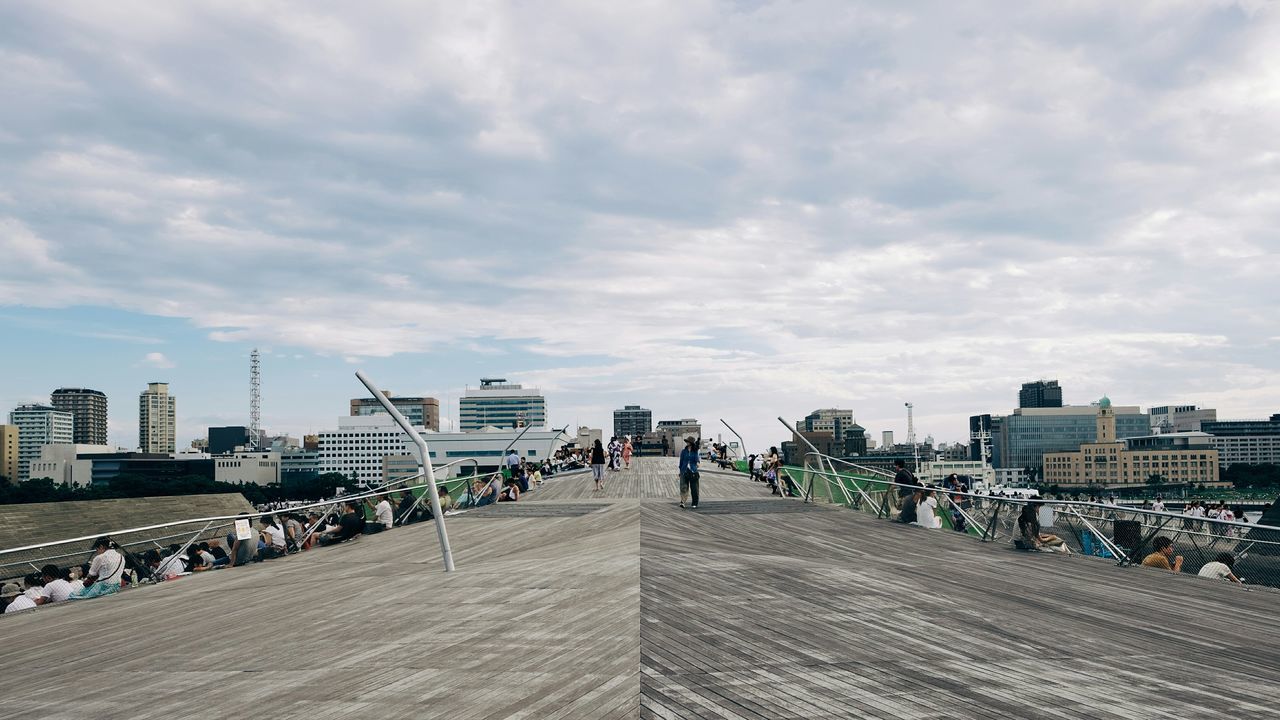 architecture, building exterior, built structure, sky, the way forward, city, cloud - sky, diminishing perspective, walkway, cloud, cobblestone, footpath, street, vanishing point, day, railing, cityscape, incidental people, road, cloudy