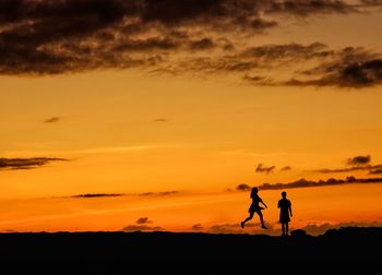 Silhouette men standing on shore against sky during sunset