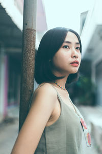 Side view of thoughtful young woman looking away while standing by pole in city