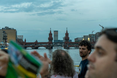 People by river in city against sky