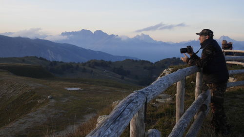 Side view of man photographing with camera on mountain against sky