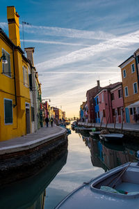 Boats moored on canal amidst buildings in city against sky