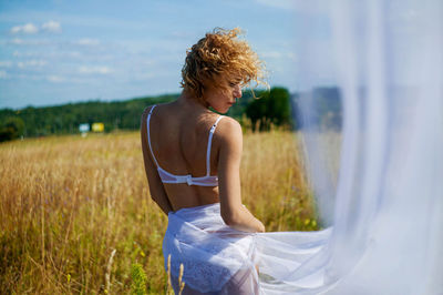 Blonde girl with curly hair in lingerie in field.