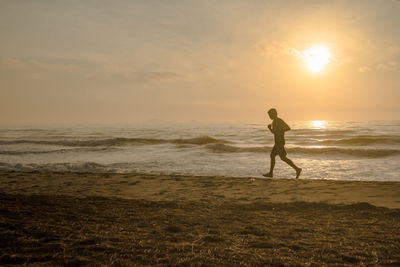 Silhouette man run on beach with sunrise and sea background