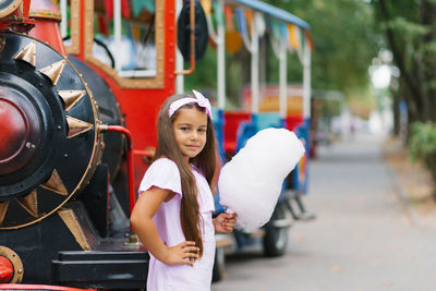 A cute dark-skinned girl in a pink dress holds cotton candy in her hands in the summer in the park