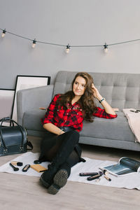 Young female makeup artist is sitting on the sofa floor next to randomly scattered brushes, makeup