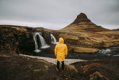 Rear view of man looking at waterfall against sky