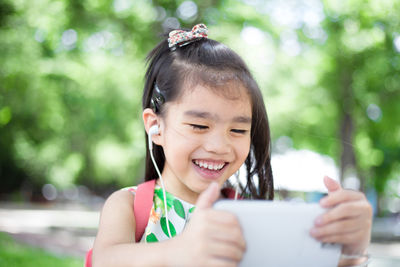 Close-up of smiling girl holding smart phone outdoors