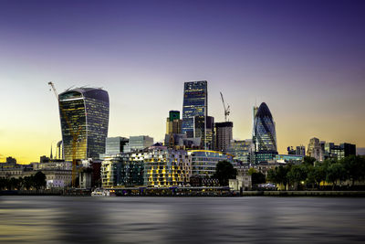 Illuminated buildings by river against sky in city