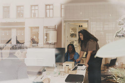 Male and female business professionals working together at office seen through glass window