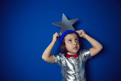 Christmas boy child holding a star in a silver shirt blue hat and red bow tie stands in the studio