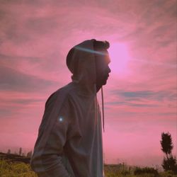 Side view of man standing on field against sky during sunset