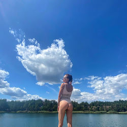 Young woman standing by lake against blue sky
