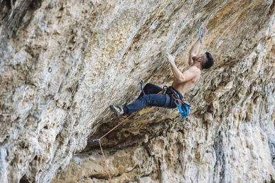 Shirtless climber sending a sport climbing route on spanish crag.