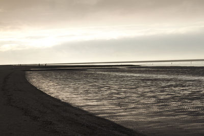 View of calm beach against cloudy sky