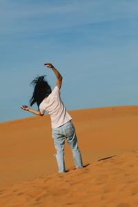 Rear view of woman standing on sand in desert against sky