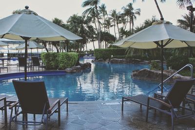 Chairs and tables by swimming pool against sky