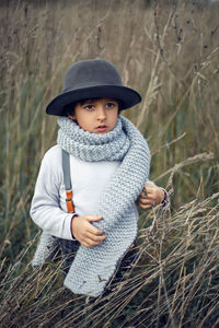 Boy child in plaid pants, hat, suspenders and scarf stands in a field in autumn