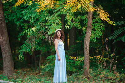 Portrait of woman standing by tree in forest