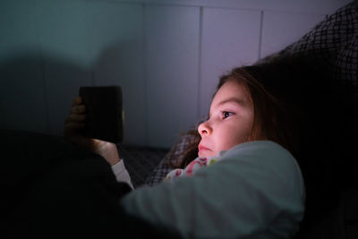 Cute girl using phone while lying on bed at night