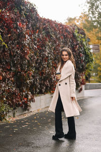 A beautiful happy girl in casual clothes is walking in the autumn outdoor park drinking coffee