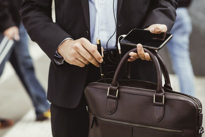 Midsection of male business person putting pen in bag while standing outdoors