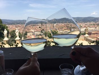 Cropped hands of people toasting wineglasses against cityscape