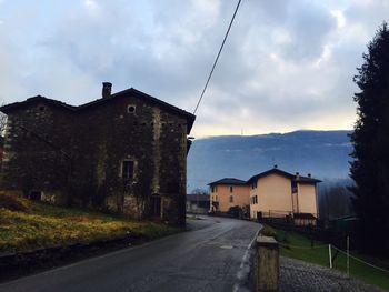 Road leading towards houses against cloudy sky