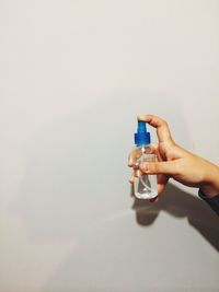 Close-up of hand holding spray bottle against wall