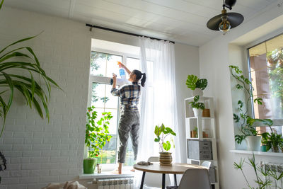 Rear view of woman standing by potted plant against wall