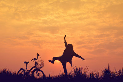 Playful woman standing by bicycle on grassy field during sunset