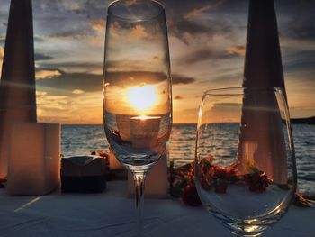 Close-up of wine glass on table against sea during sunset