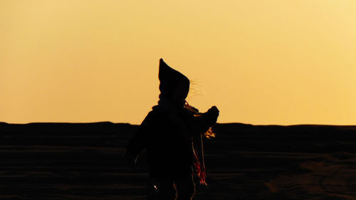 Rear view of silhouette man standing on land against sky during sunset